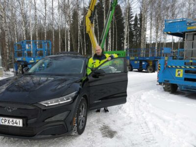 Mies seisoo mustan auton oven takana vuokraamon lumisella pihalla.