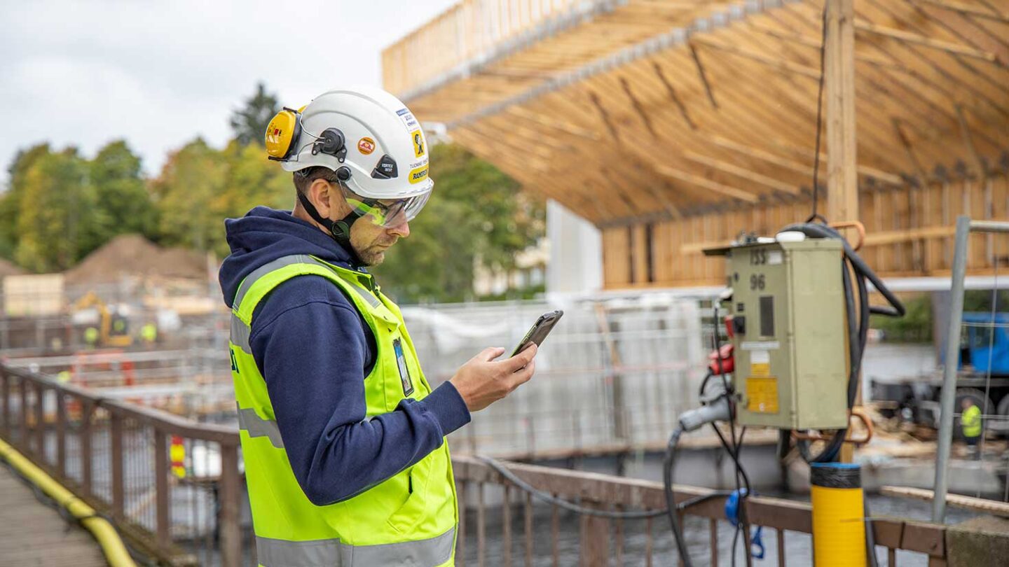 Henkilö selaa puhelinta työmaalla.