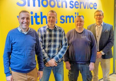 Neljä miestä seisoo rivissä keltaisen taustan edessä.