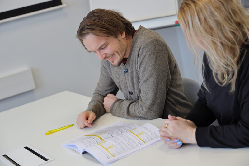 Mies ja pitkähiuksinen nainen istuvat pöydän ääressä tutkimassa papereita.