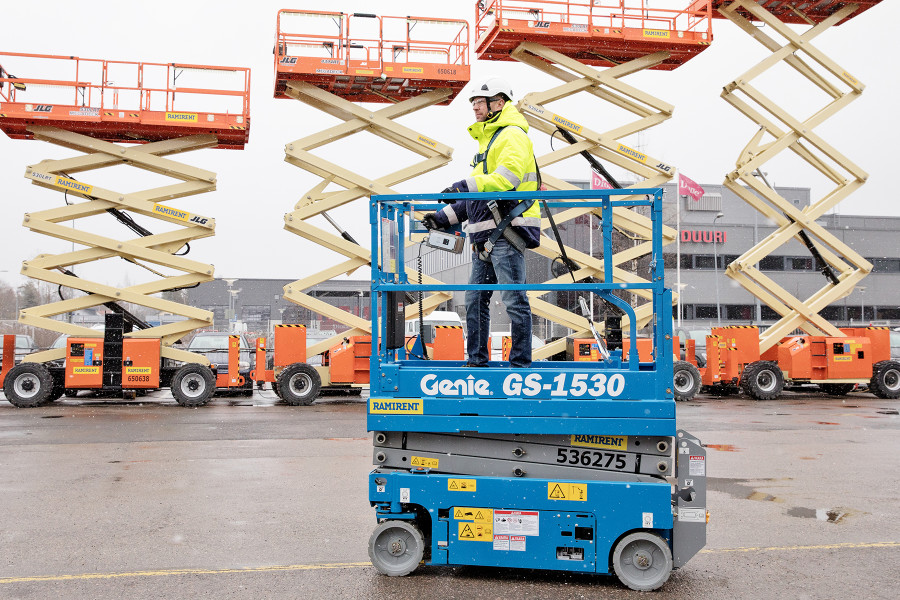 Mies Genie GS-1530 nostimen kyydissä. Taustalla useita JLG:n nostimia yläasennossa.