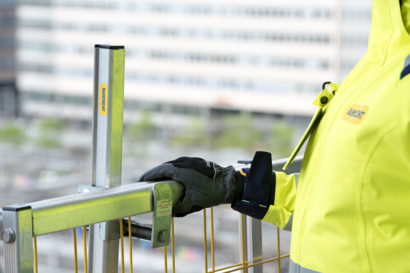 Mustaan työhansikkaaseen puettu käsi pitää kiinni metallisesta suojakaiteesta.