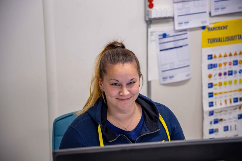 Rhea istuu työpisteellään ja hymyilee.