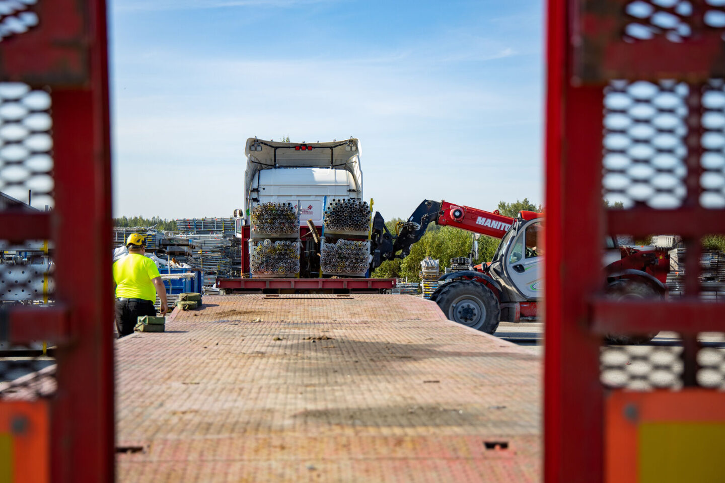 Perälautojen välistä katsottuna lastataan telinehäkkejä rekan kyytiin.