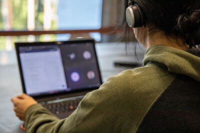 Nainen käyttää tietokonetta kuulokkeet päässä.