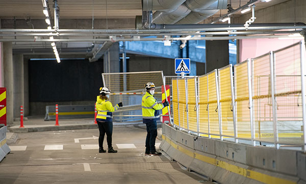 Kaksi työmaapukuista ihmistä asentaa SafePass-turvakaidetta hallissa.