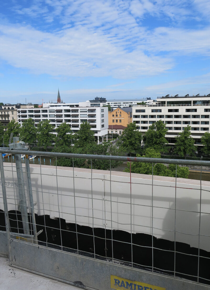 Näkymä rakennuksen katolta Aurajoen yli kaupunkiin. Etualalla on katon reunalla putoamisen estävä suojakaide.