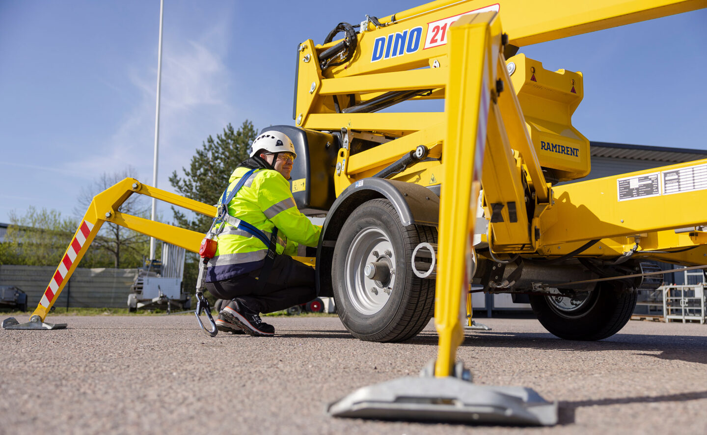Kypäräpäinen mies on kyykistyneenä keltaisen henkilönostimen vierellä.