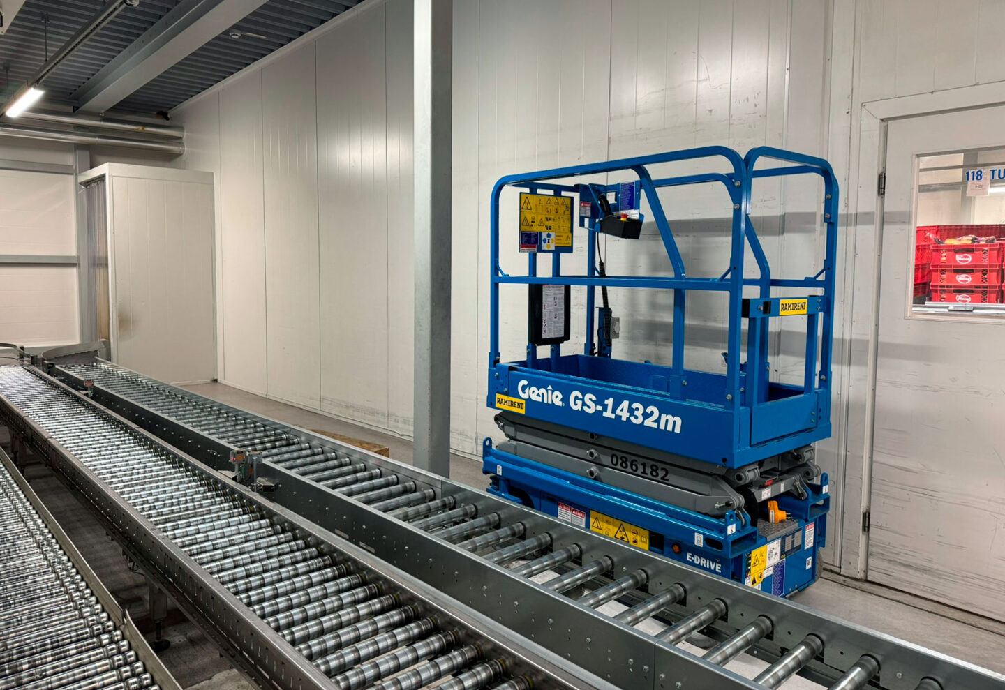 Sininen saksinostin kuvattuna leipomossa kuljetushihnan takana.