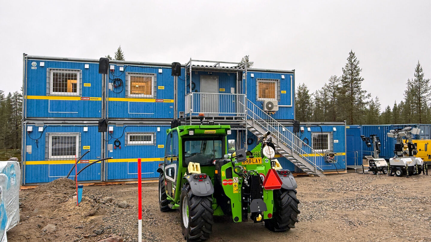 Vihreä kurottaja seisoo työmaalla kahteen kerrokseen asennettujen sinisten työmaatilojen edessä.