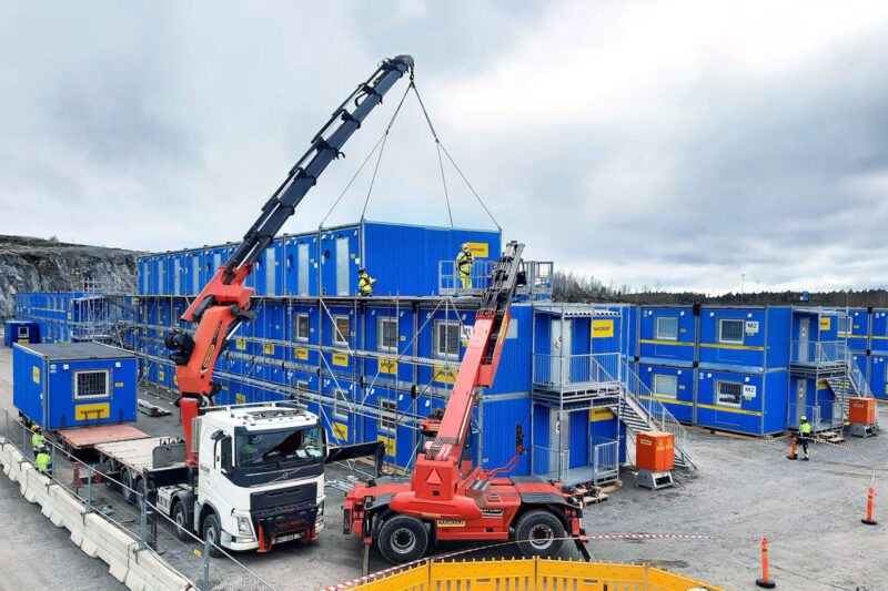 Ramirentin sinisiä työmaatiloja asennetaan kolmeen kerrokseen autonosturin ja kurottajan avulla.