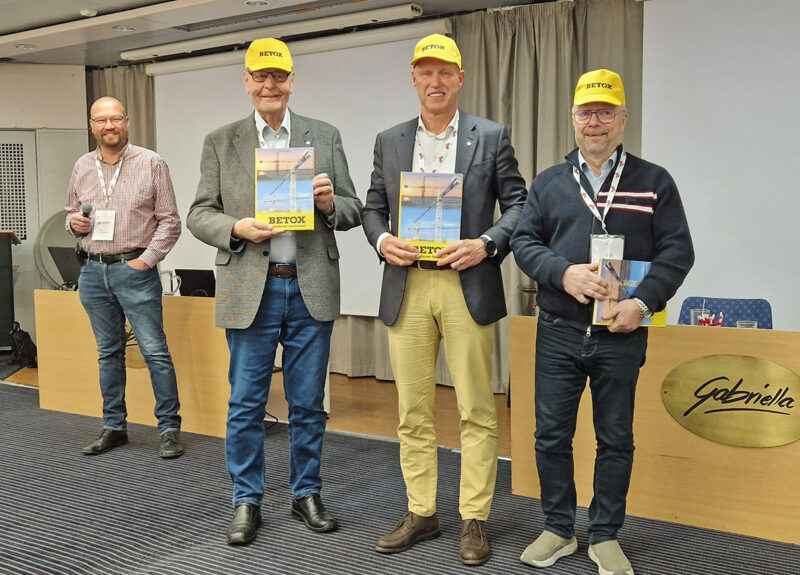 Neljä miestä seisoo rivissä ja pitelee käsissään kirjaa.