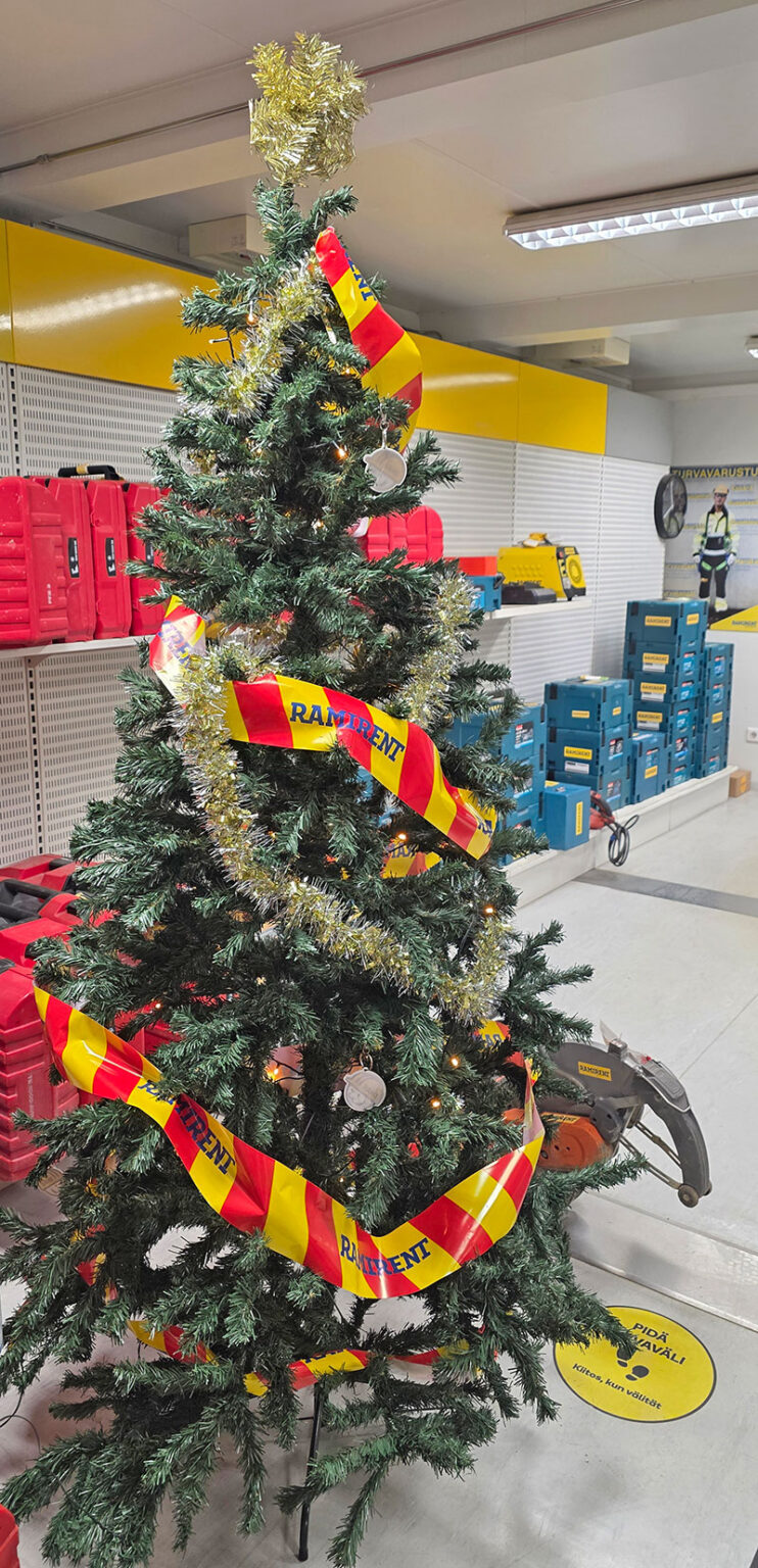 Eristysnauhalla ja kimalleköynnöksellä koristeltu joulukuusi konevuokraamon hyllyjen edessä.
