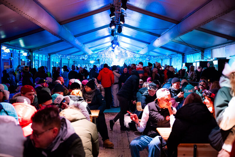 Sinisävyinen kuva ihmisjoukosta suuren tapahtumateltan sisällä.