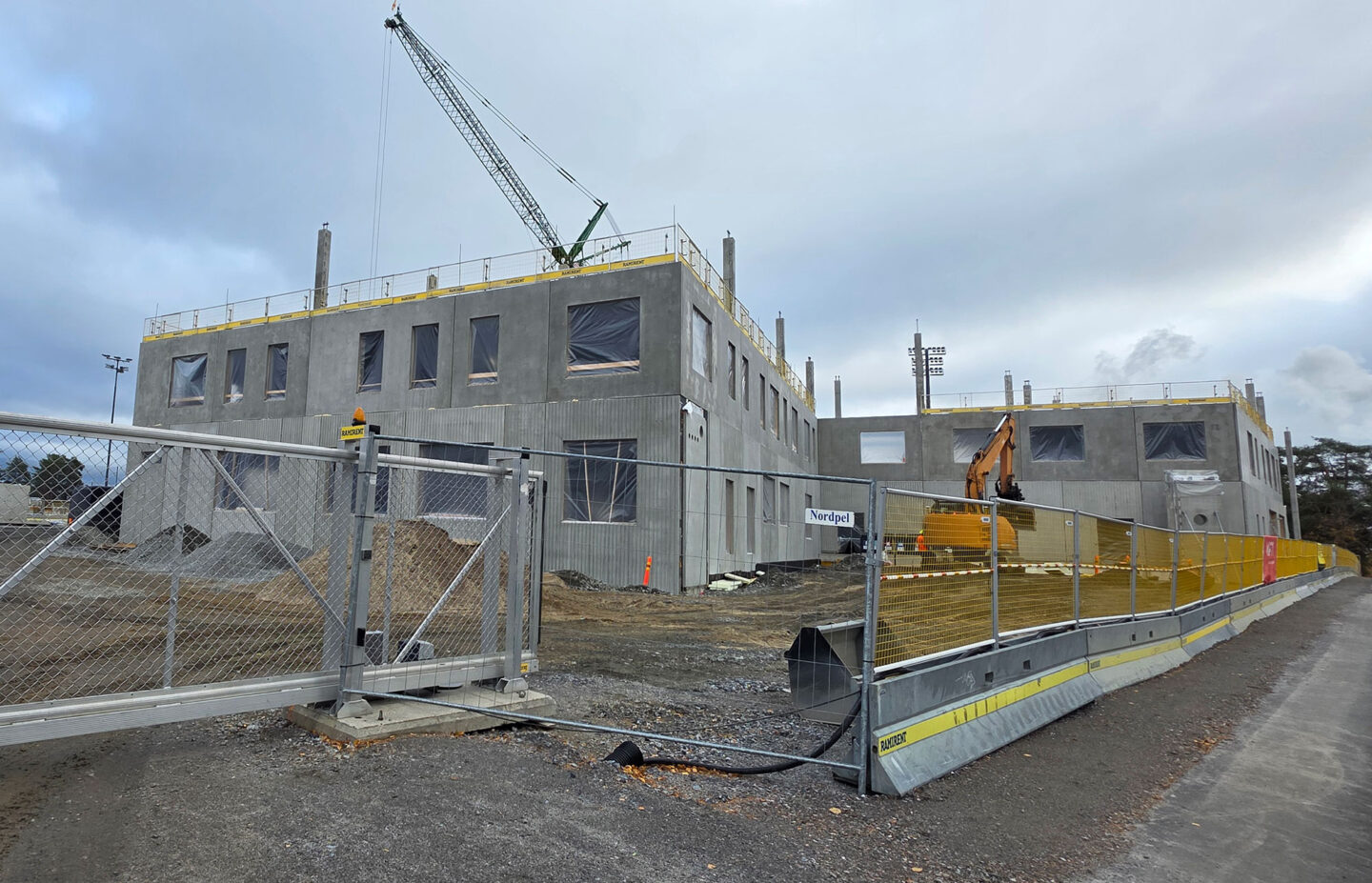 Rakenteilla oleva betoninen kaksikerroksinen koulu jonka edessä on työmaa-aita ja liukuportti.