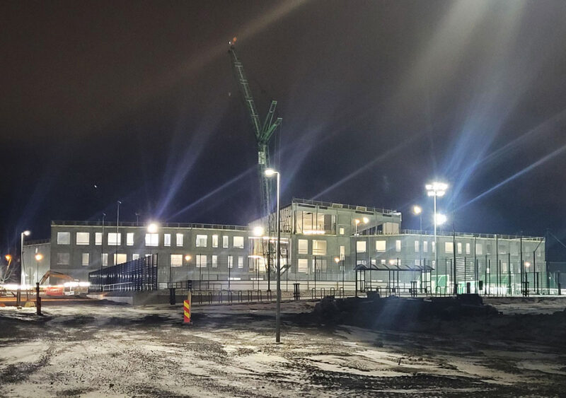 Rakenteilla oleva betoninen koulurakennus kuvattuna illalla valojen ollessa päällä.
