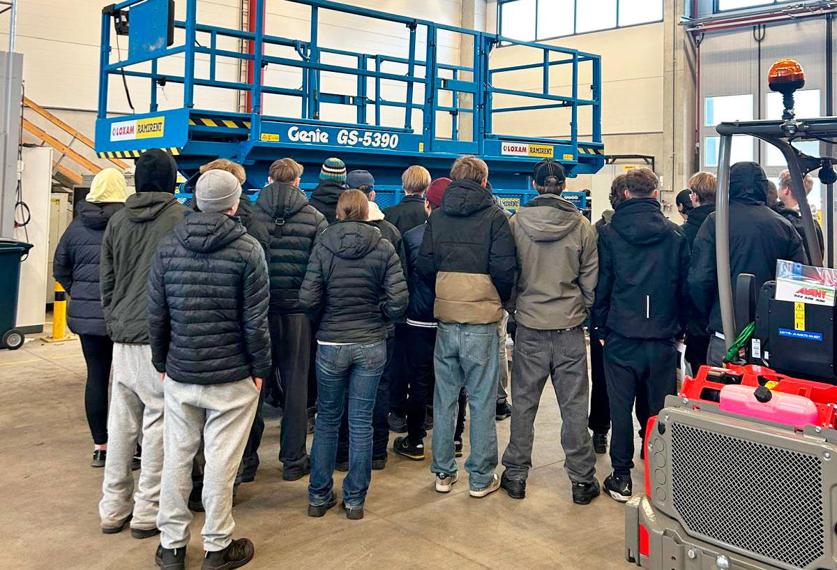 Joukko nuoria opiskelijoita seisoo saksinostimen ympärillä konevuokraamon hallissa.