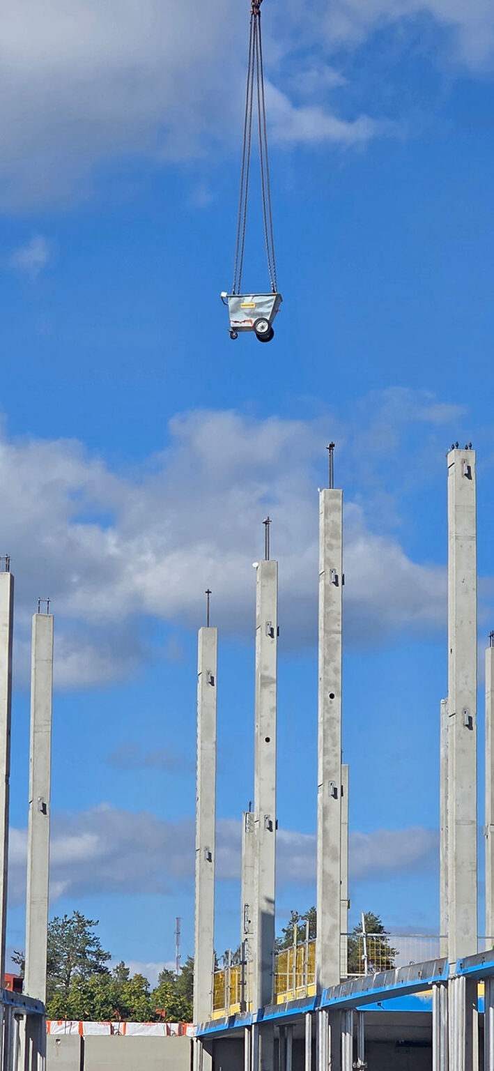 Roskavaunu roikkuu työmaan palkkien yläpuolella nosturin nostamana.