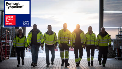 Joukko työvaatteisiin pukeutuneita ihmisiä kävelee kohti kameraa varastohallissa.