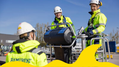 Kuvassa on kaksi miestä nostimen korissa ja nainen selin kameraan ja kuvan alareunassa on keltainen aaltokuvio.