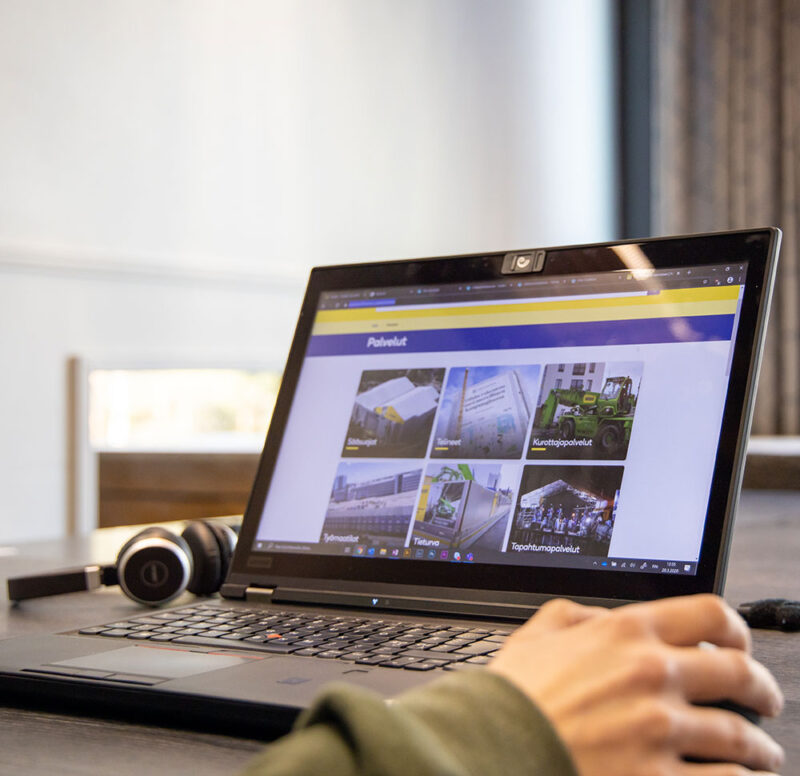 Pöydällä on kannettava tietokone ruutu avoinna sekä hiirtä pitelevä käsi.