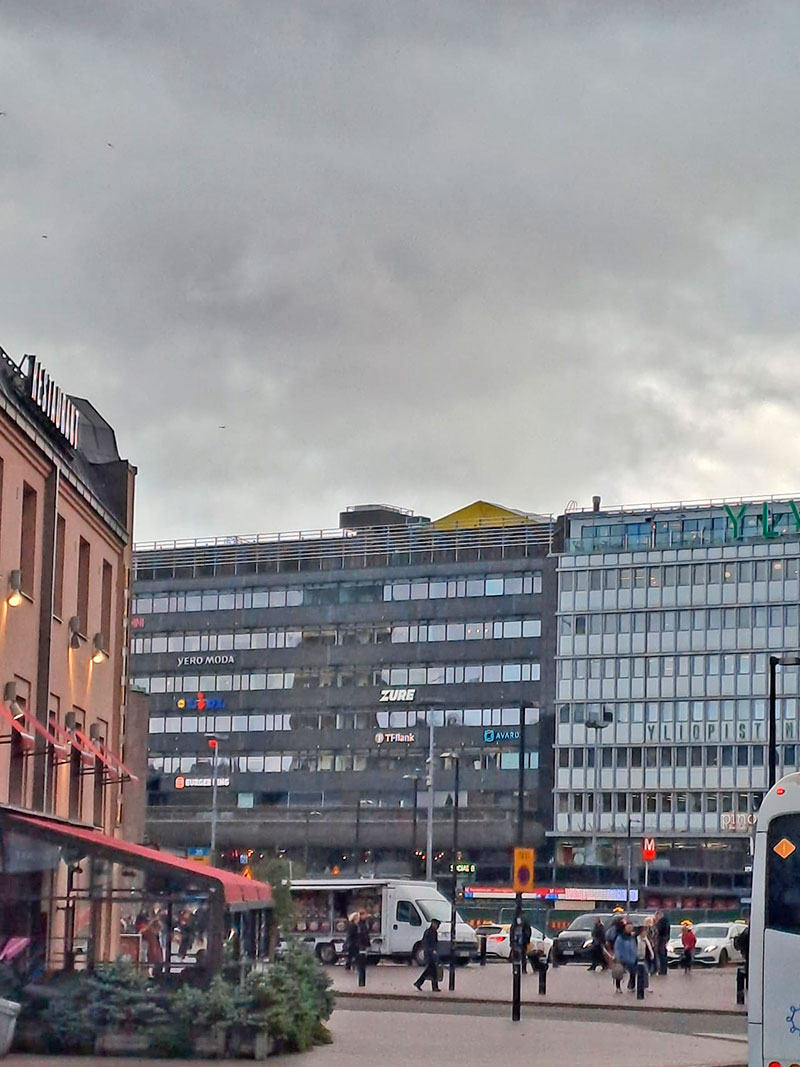 Ramirentin keltainen sääsuojan pääty pilkottaa kattojen takaa rakennuksen sisäpihalta.